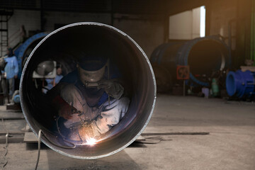 A welder welds large diameter pipes with manual electric arc welding