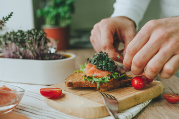 Man making sandwich with salmon fish, microgreen and tomato
