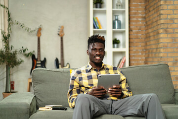 Cheerful young man paying bills online with credit card and digital tablet. African man using credit card at home.