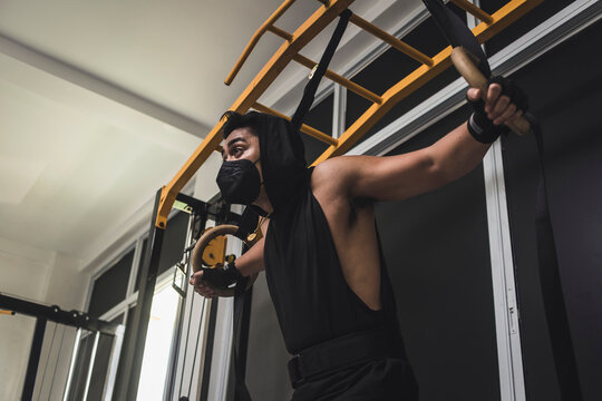 A hooded man doing chest flyes using wooden still rings at the gym. Calisthenics exercises on gymnastics rings.