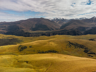 Mountain peaks covered with snow at the top and dry grass below and with clouds descending on the...