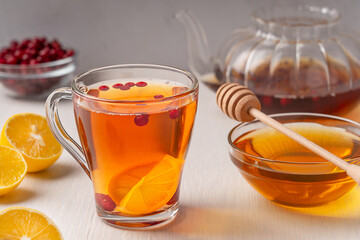 Traditional homemade herbal hot tea made with sour lemon citrus slices, cranberries and sweet honey served in glass cup on white wooden table with ingredients and teapot as winter vitamin drink