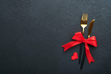 Valentines day romantic table setting. Empty or closeup of a dinner black plate, knife, fork and decorative silk hearts on black background. Holiday concept. Copy space for inscriptions.