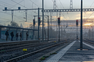 Commuters waiting at railroad platform at railway station of Swiss City Biel Bienne on a sunny foggy autumn morning. Photo taken November 10th, 2022, Biel Bienne, Switzerland.