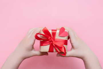 a gift in eco style with craft paper and a red ribbon on a pink background with a heart in...