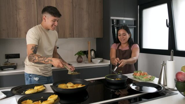 Two young latin people cooking llapingachos and eggs in a pan at kitchen.