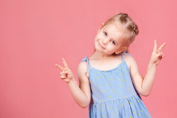маленькая веселая девочка на розовом фоне показывает знак победы.a little cheerful girl on a pink background shows a victory sign