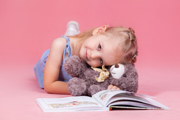 a little girl with a teddy bear reads a book lying on the floor