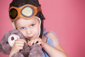 a little girl in a pilot's helmet hugs a teddy bear