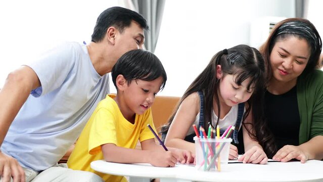 Asian father and mother looking children drawing a picture at home.