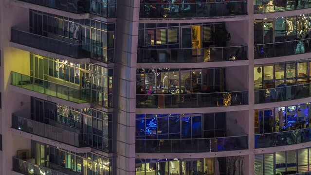 Night view of exterior apartment colorful building timelapse. High rise skyscraper with glowing lights in windows. Chairs on a balconies