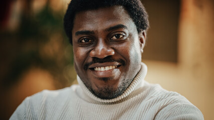 Close-up Portrait of Handsome Black Man with Trimmed Beard, Wearing Stylish White Turtleneck, Smiling and Looking at the Camera. Confident Male Startup CEO Celebrating his Achievement