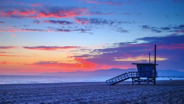 Colorful sunset over ocean in Venice Beach, Santa Monica, Los Angeles, California. Zoom in on lifeguard tower. 4K Timelapse.
