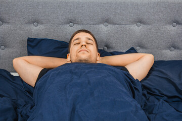 Top view of a handsome young man sleeping comfortably on the bed in his bedroom at night. Bachelor bedroom. Deep sleep.