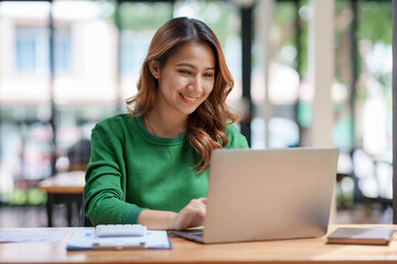 Attractive Asian businesswoman using laptop in office working attentively and happily. - obrazy, fototapety, plakaty
