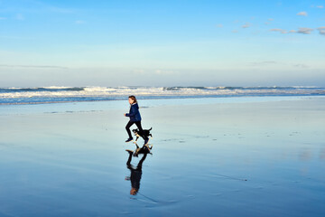 Beautiful young girl running with her border collie puppy on the beach at dawn