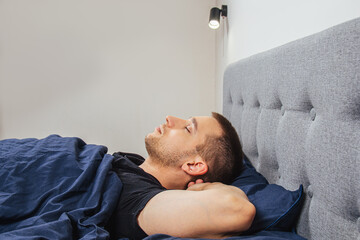 Top view of a handsome young man sleeping comfortably on the bed at night in his bedroom. Sleep in...