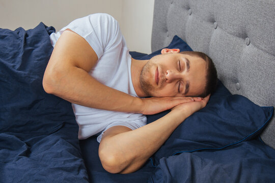 Top View Of A Handsome Young Man Sleeping Comfortably On The Bed At Night In His Bedroom. Sleep In Different Positions. Bachelor Bedroom. Deep Sleep.