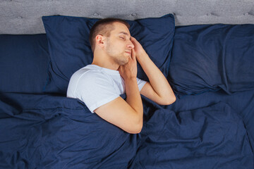 Top view of a handsome young man sleeping comfortably on the bed at night in his bedroom. Sleep in different positions. Bachelor bedroom. Deep sleep.