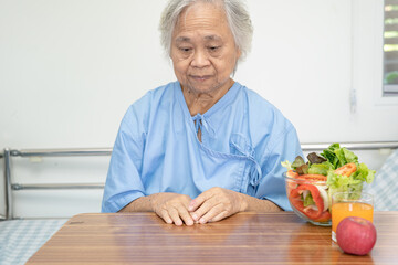 Asian senior or elderly old lady woman patient eating Salmon steak breakfast with vegetable healthy food while sitting and hungry on bed in hospital.