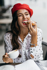 Young stylish woman in red beret having a french breakfast with coffee and croissant sitting oudoors at the cafe terrace. Fresh Baked Croissants. 