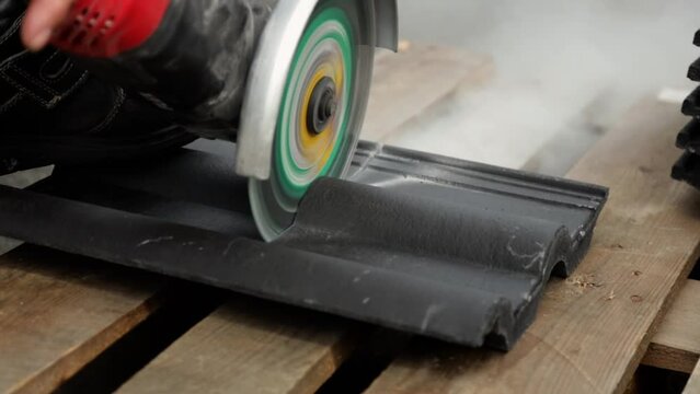 Dachdecker schneidet Dachziegel durch mit einer Flexmaschine 