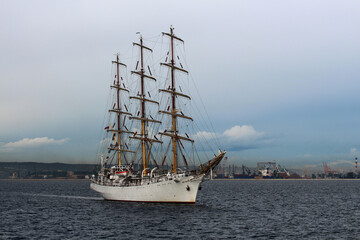 Naklejka na ściany i meble Three-masted sailing frigate goes to sea from the port against a stormy sky.
