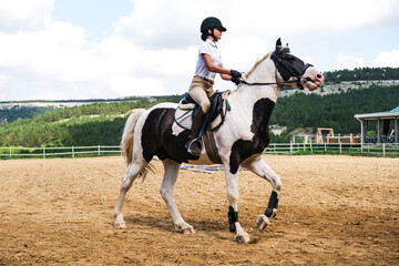 A young girl on a spotted horse is engaged in show jumping outdoors.