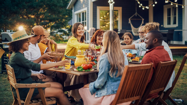 Family And Multiethnic Diverse Friends Gathering Together At A Garden Table. People Eating Grilled And Fresh Vegetables, Sharing Tasty Salads For A Big Family Celebration With Relatives.