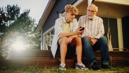Handsome Teenage Grandson Teaching His Grandfather to Use a Smartphone. Young Man Showing Family...