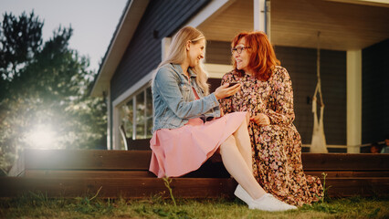 Beautiful Teenage Granddaughter Teaching Her Grandmother to Use a Smartphone. Girl Showing Family Photos and Videos to Her Grandparent. Relatives Sitting Outside on a Porch on a Warm Summer Day.