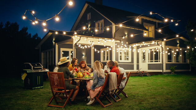 Group of Multiethnic Diverse People Having Fun, Communicating with Each Other and Eating at Outdoors Dinner. Family and Friends Gathered Outside Their Home on a Warm Summer Evening.