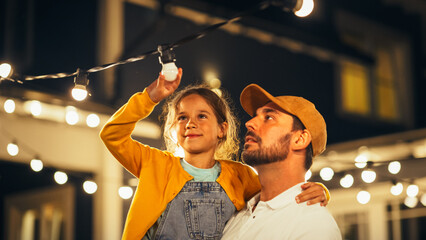 Happy Handsome Father Helping His Little Beautiful Daughter to Change a Lightbulb in Fairy Lights...