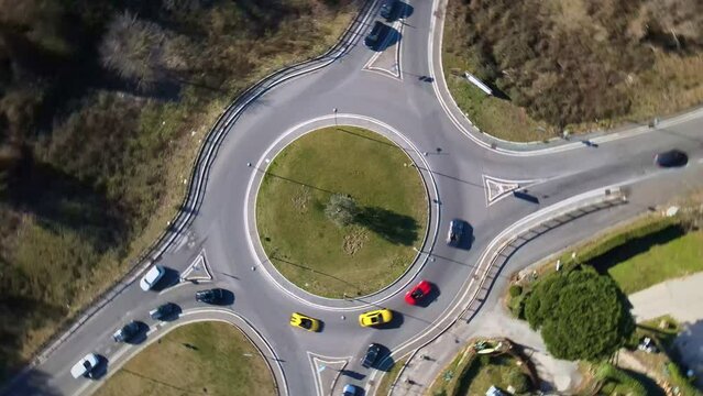 Road junction with roundabout and different directions, premium class sports cars driving inside the green roundabout in traffic time, aerial view of driving super sports cars in roundabout