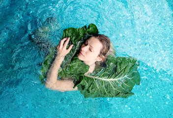 sensual seductive young woman nestles in the water against a large green plant leaf, in spa...