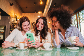 Three ladies smiling and having fun using a cellphone to send text messages at restaurant or coffee...