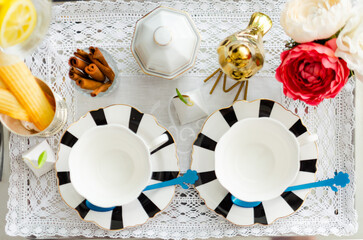 Black and white stripes porcelain tea sets, including teacups, plates, spoons and sugar bowl on a silver tray covered with lace, decorated with tulips, a golden bird, cinnamon and lime