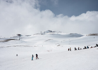 Fototapeta na wymiar Skiers go downhill skiing on snow-covered mountain ski slope against the backdrop of a cloudy sky and ski lifts. Winter. Extreme sport and travel content 