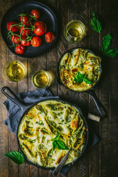 Baked Pasta in two skillets with roasted tomatoes, wine glasses and basil