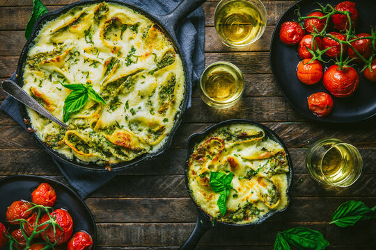 Baked Pasta in two skillets with roasted tomatoes, wine glasses and basil