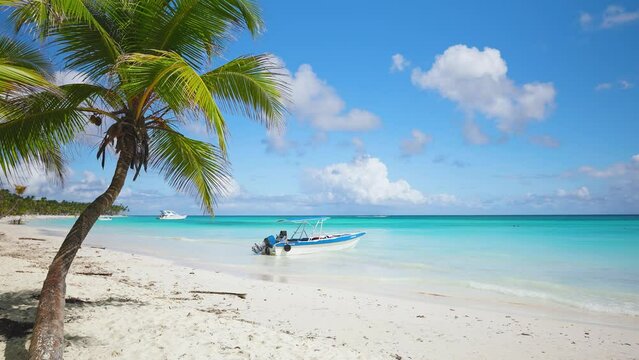 Sunny, idyllic Kendwa beach with white sand and vibrant green palm trees. White boat on the turquoise water of the ocean off the coast of Zanzibar. Landscape of sea beach under blue cloudy sky.