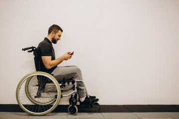 The disabled person sits in a wheelchair. He is talking to someone on his smartphone. He is in his large bright living room. He smiles.