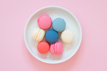 Fototapeta na wymiar Vibrant colored macaroon cookies served on white plate, pink background, top view