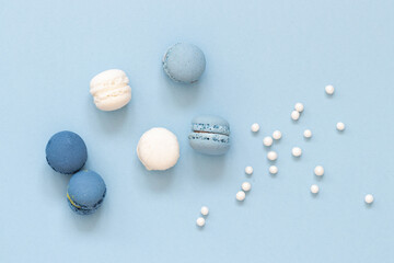 Blue and white macaroon cookies with sugar pearls arranged on blue background, top view, horizontal