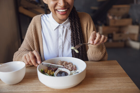 Cropped view to African woman smiling toothy smile, holding cutlery and tasting healthy diet food at gourmet restaurant