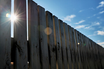 An old wooden fence against a blue sky with clouds on a sunny day. Background of old wooden boards in rustic style