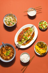 European sea bass or Spigola fish steamed with ginger, red peppers in soy sauce served  with Chinese cabbage, traditional spicy soup and rice. Chinese New Year, festive table in Cantonese style