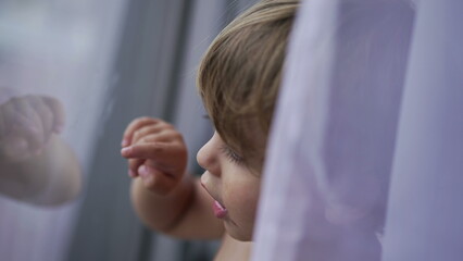 Child standing by window glass pointing with finger, toddler 2 year old baby