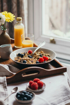 Breakfast tray with granola, berries and juice next to a window