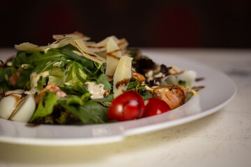 Salad with shrimp and tomatoes, cheese and herbs on a plate in a restaurant